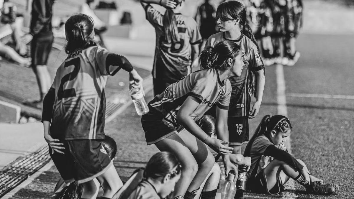 Young female soccer team resting on the sidelines during a match in black and white.
